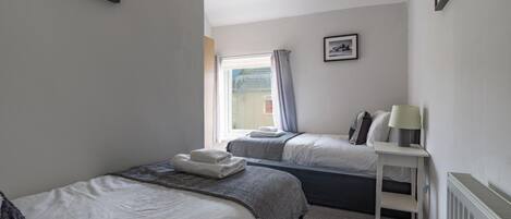 Camera d'albergo con due letti, un comodino con lampada, un termosifone e una finestra con tende.