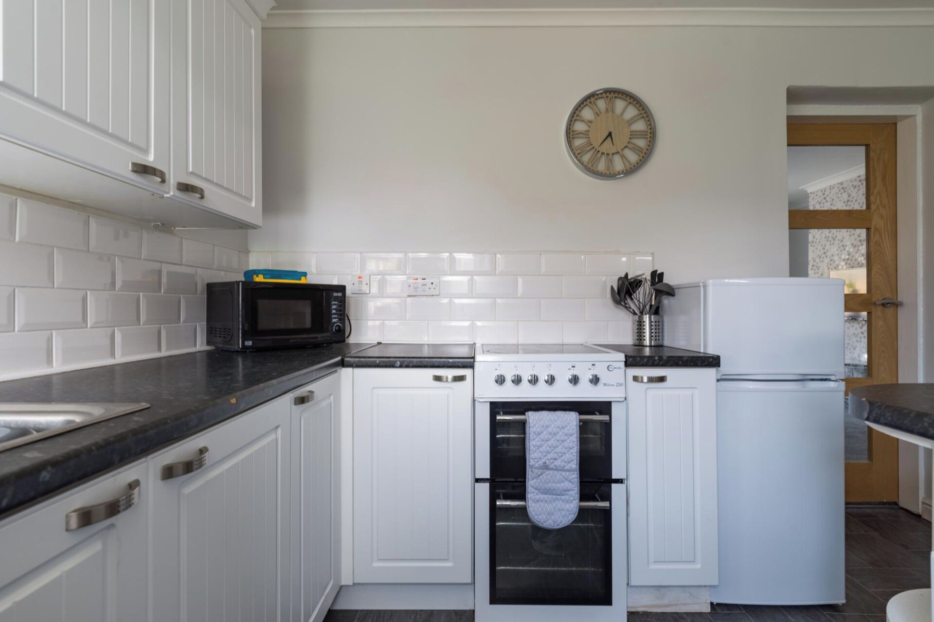 Una cucina con mobili bianchi, un forno a microonde nero, un piano cottura bianco e un frigorifero bianco.