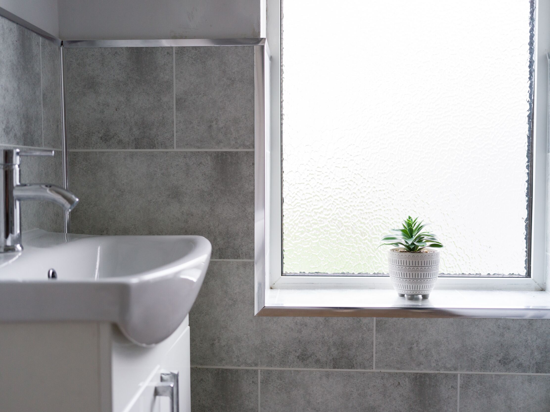 A bathroom with a white sink, a faucet, and a window with a potted plant on the sill.