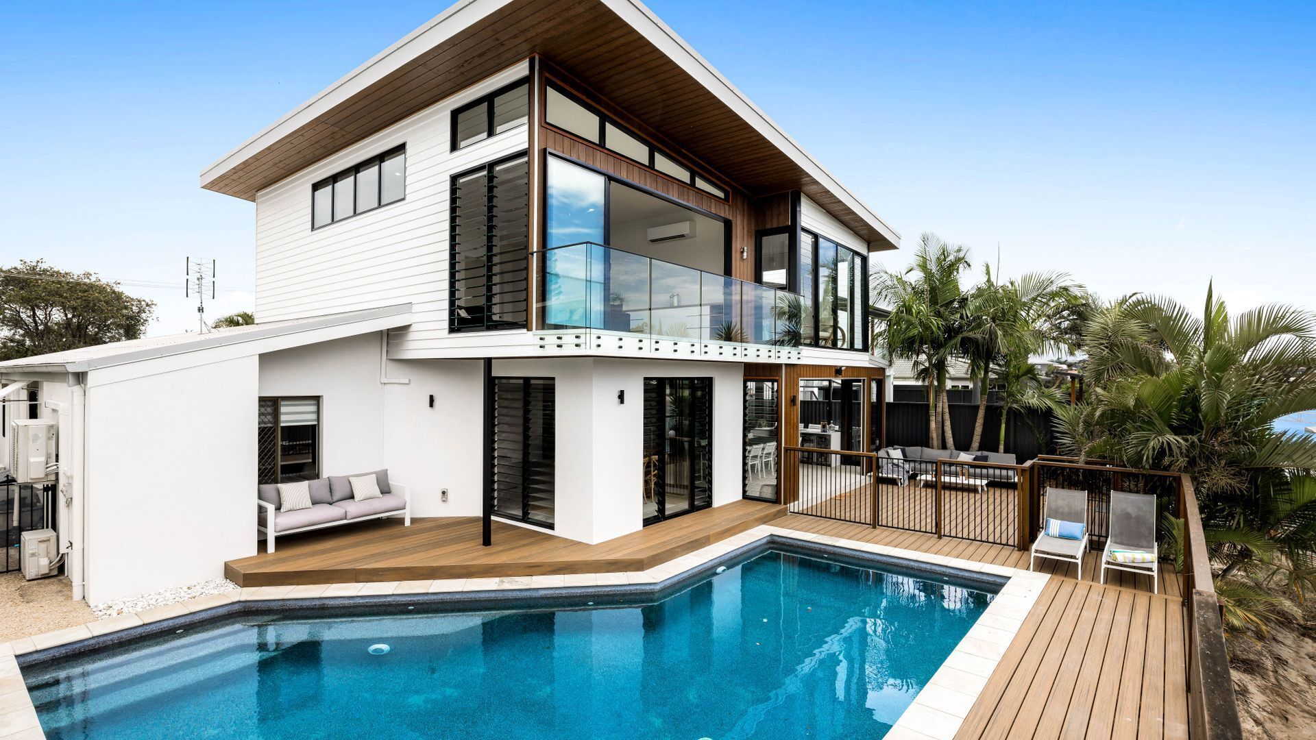 A modern two-story house with a swimming pool, a deck, and a balcony overlooking the pool.