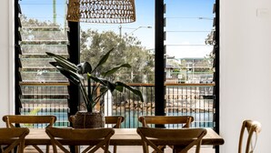 Un comedor con mesa y sillas de madera, una planta en maceta y vista a una costa rocosa a través de amplios ventanales.