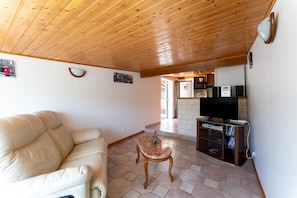 A living room with a wooden ceiling, a sofa, a coffee table, a television, and a bookshelf. - Holiday Home 'Villa du Soleil Levant' with Mountain View, Wi-Fi & Air Conditioning (Apt)