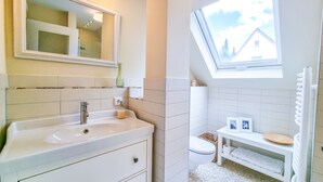 A bathroom with a white sink, mirror, and toilet. There is a window with a view of a house and trees. - Luxurious apartment * Air conditioning * Parking lot (Coburg)