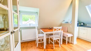 A small dining area with a wooden table and white chairs, a window with a view of greenery, and a kitchen area with cabinets and a countertop. - Luxurious apartment * Air conditioning * Parking lot (Coburg)