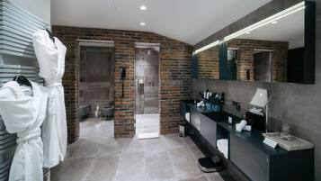 Une salle de bain moderne avec un mur en briques, un grand miroir, un meuble-lavabo avec des articles de toilette et un espace douche.