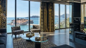 Ein modernes Wohnzimmer mit großen Fenstern, einem Glastisch, gemusterten Sofas und Blick auf das Meer und die Berge.
