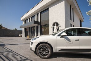 A modern villa with a white exterior, a statue near the entrance, and a white car parked in front. - Villa Geba Boutique Hotel (Sveti Stefan)