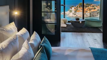 Une chambre moderne dotée d’un grand lit, d’un coin salon avec une table ronde et d’un balcon offrant une vue sur la mer et les bâtiments.
