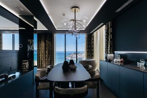 A modern dining area with a view of the sea, a chandelier, and a bar with glassware.