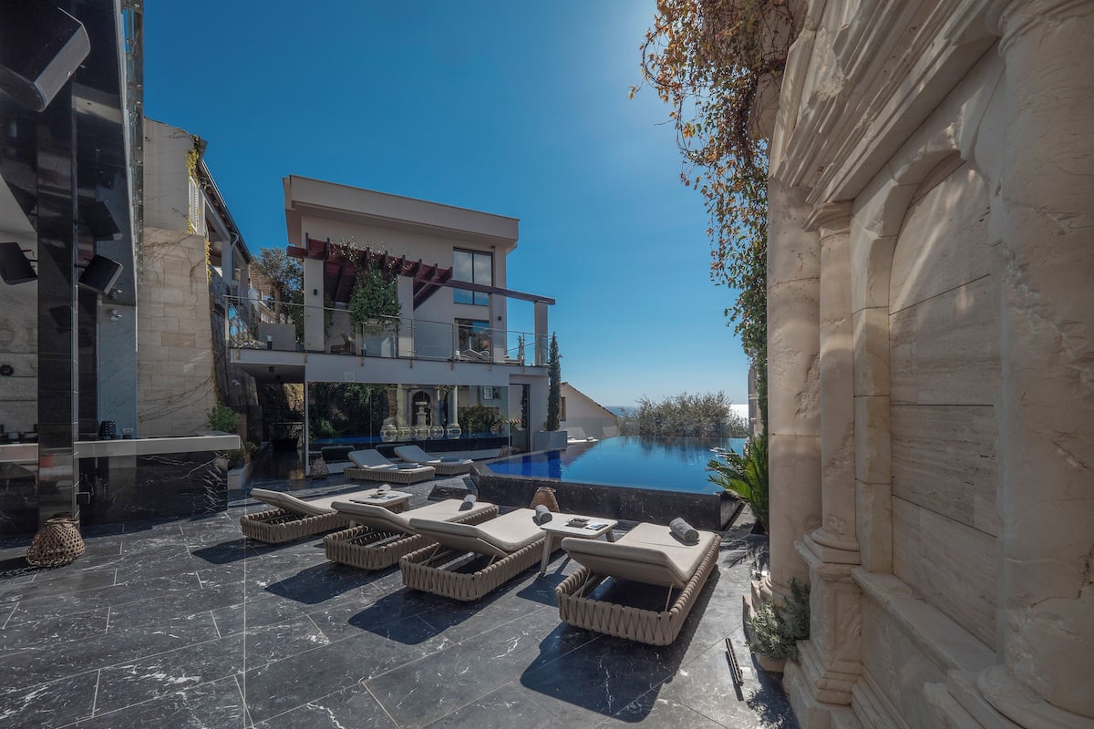 A modern outdoor pool area with lounge chairs and a clear view of the sea.