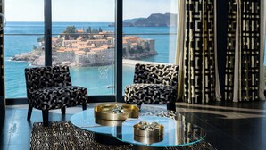 A modern living room with a glass coffee table, patterned armchairs, and a view of a coastal town. - Villa Geba Boutique Hotel (Sveti Stefan)