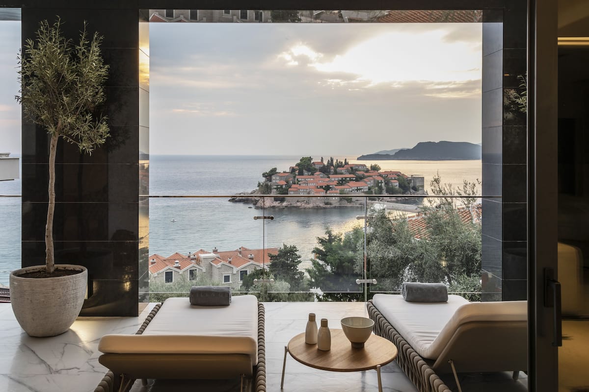A balcony with a view of a coastal town, a potted plant, and a seating area with a table.
