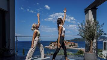 Dos personas practicando yoga en un balcón con una vista panorámica del mar y edificios.