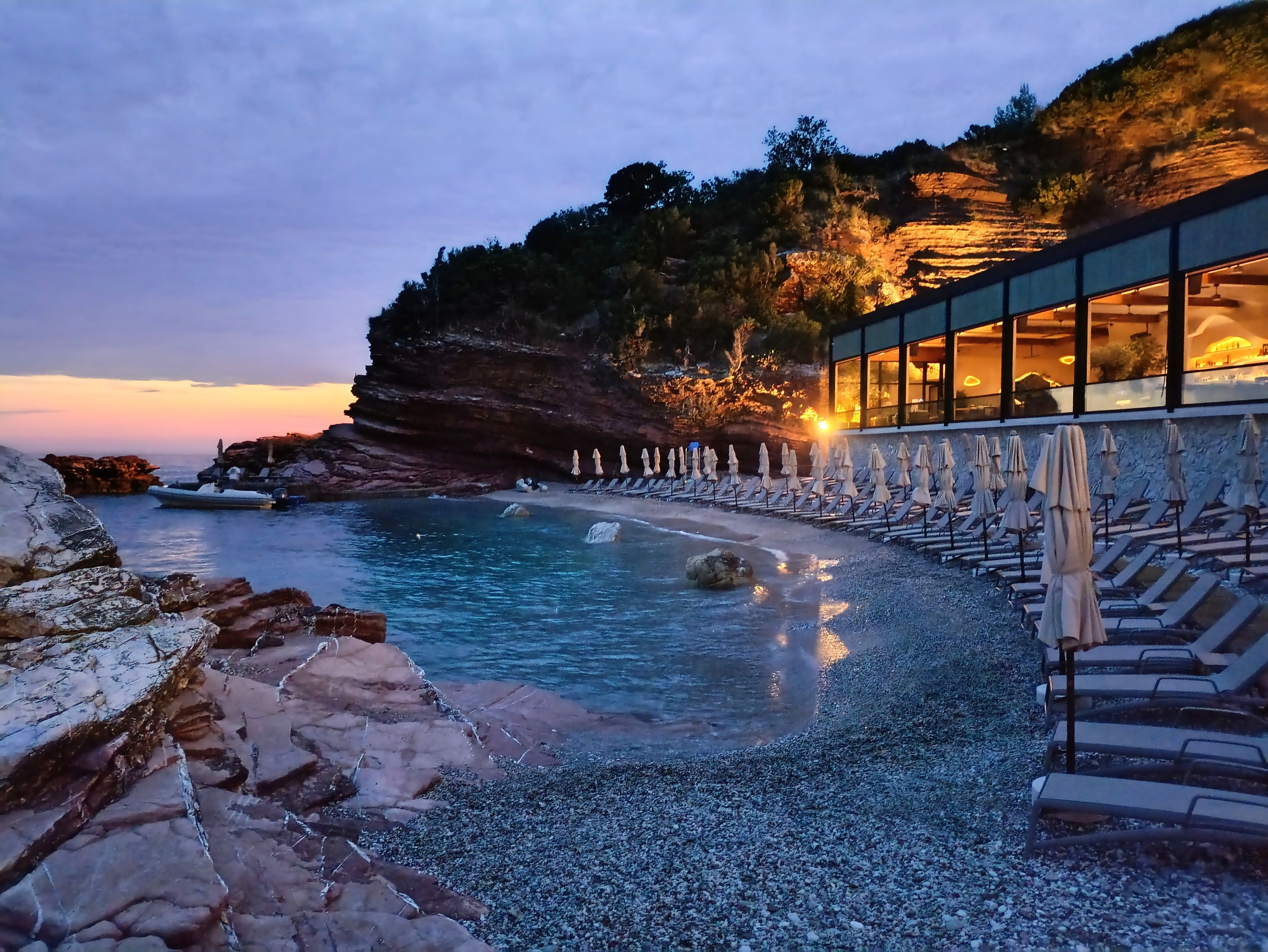 Un hotel sul lungomare con spiaggia di ciottoli, costa rocciosa e area relax interna in vetro.