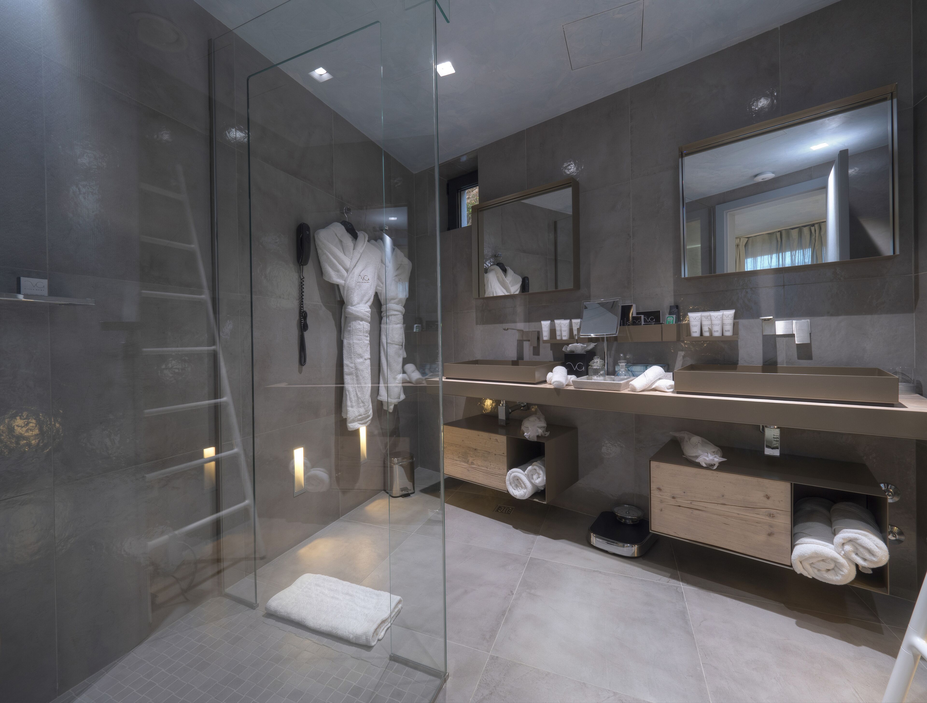 A modern bathroom with a glass-enclosed shower, a vanity with a large mirror, and neatly arranged towels and toiletries.