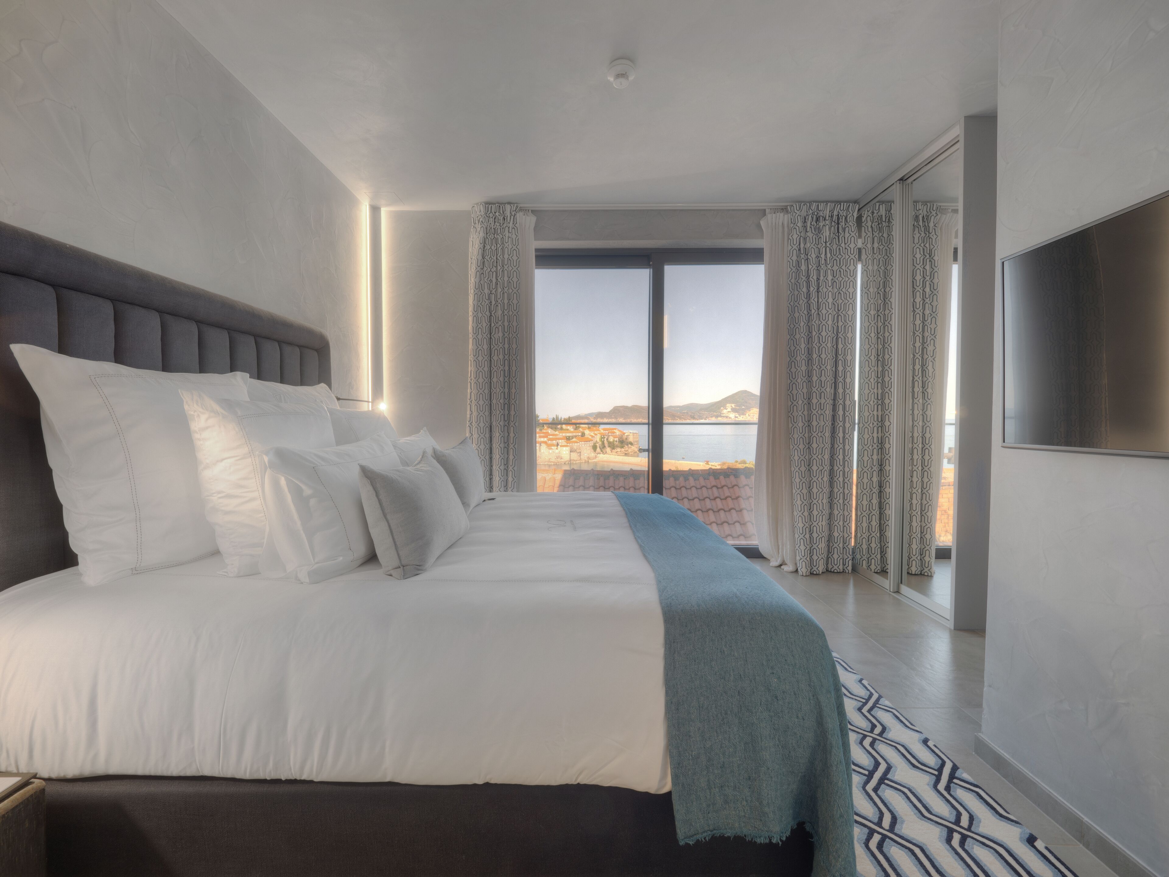 Une chambre d’hôtel moderne dotée d’un grand lit, d’un téléviseur à écran plat et offrant une vue sur le paysage urbain et l’eau.