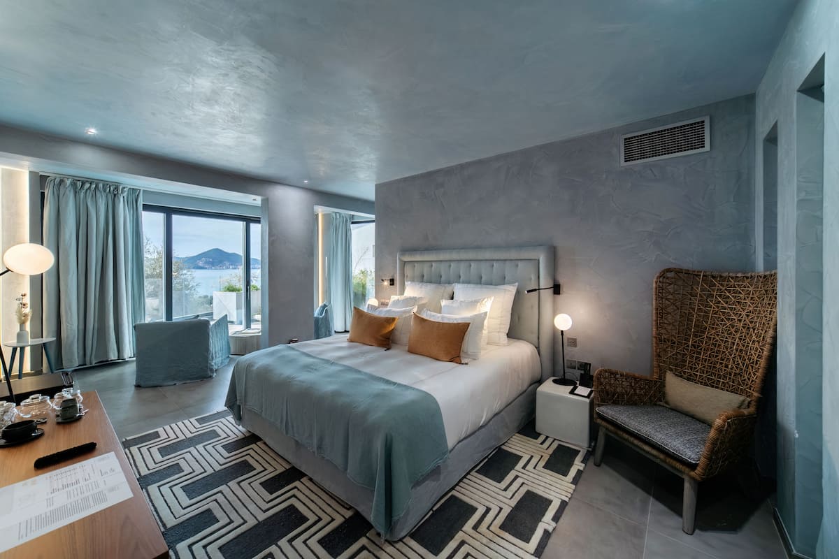 A modern hotel room with a large bed, a chair, a desk, and a view of the outdoors.