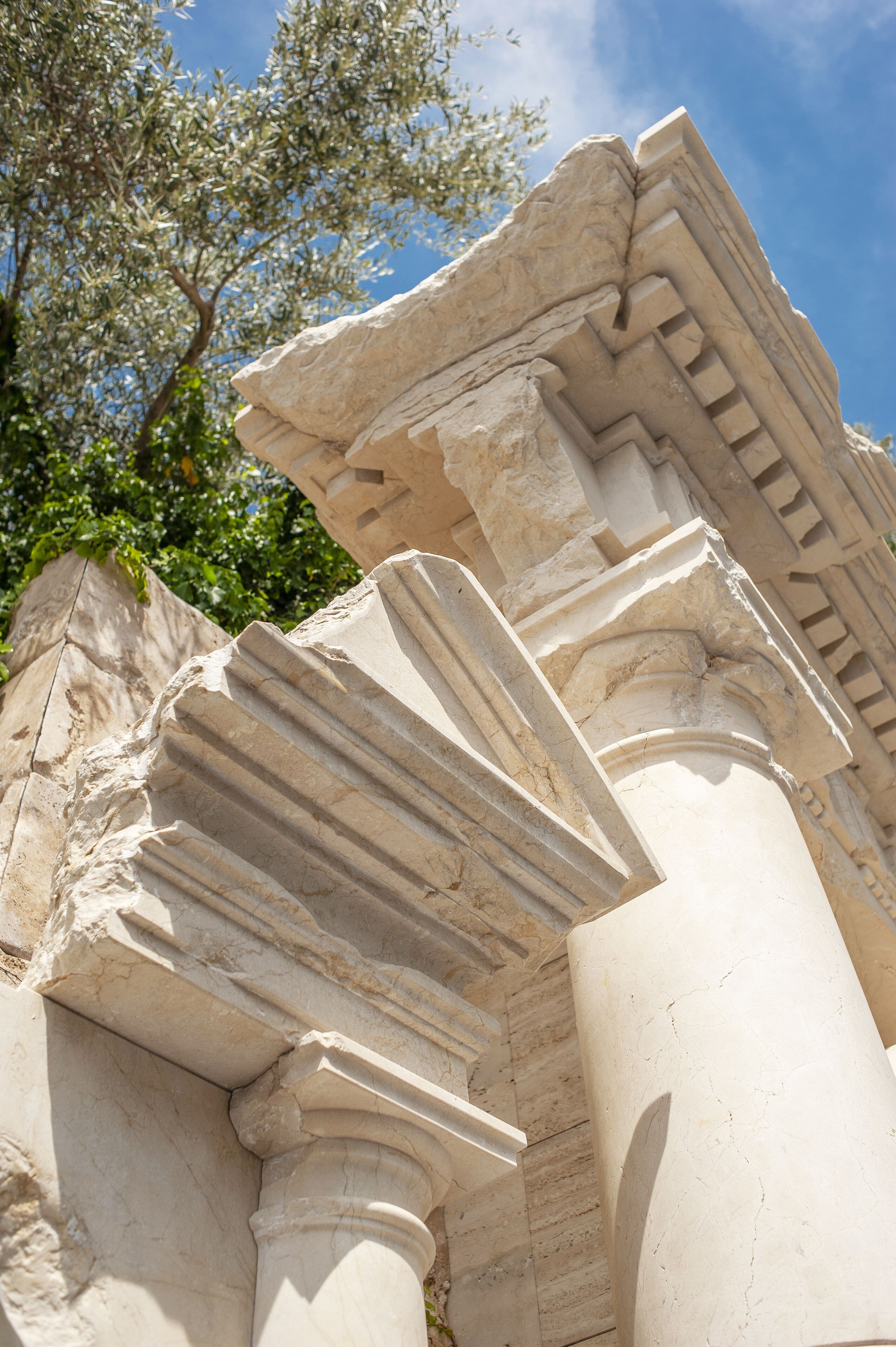 A close-up of ancient stone columns with intricate carvings, set against a backdrop of a clear sky and green foliage.