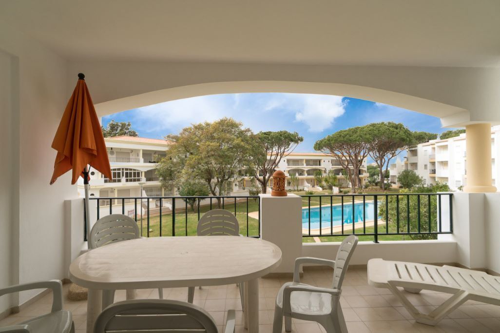 Ein Balkon mit Tisch und Stühlen, Blick auf einen Swimmingpool und ein Gebäudekomplex im Hintergrund.