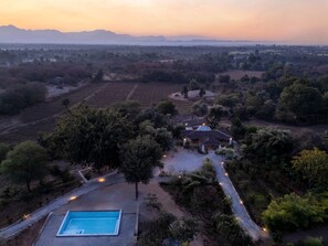 Vista aérea de una propiedad con piscina, rodeada de árboles y campos, con una casa en el centro.