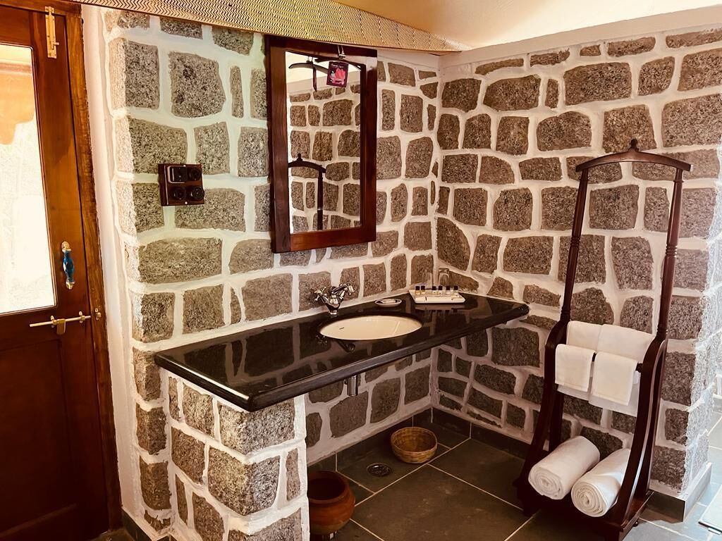 Une salle de bain avec des murs en pierre, un plan de travail noir, un lavabo, un miroir, un porte-serviettes et une douche.