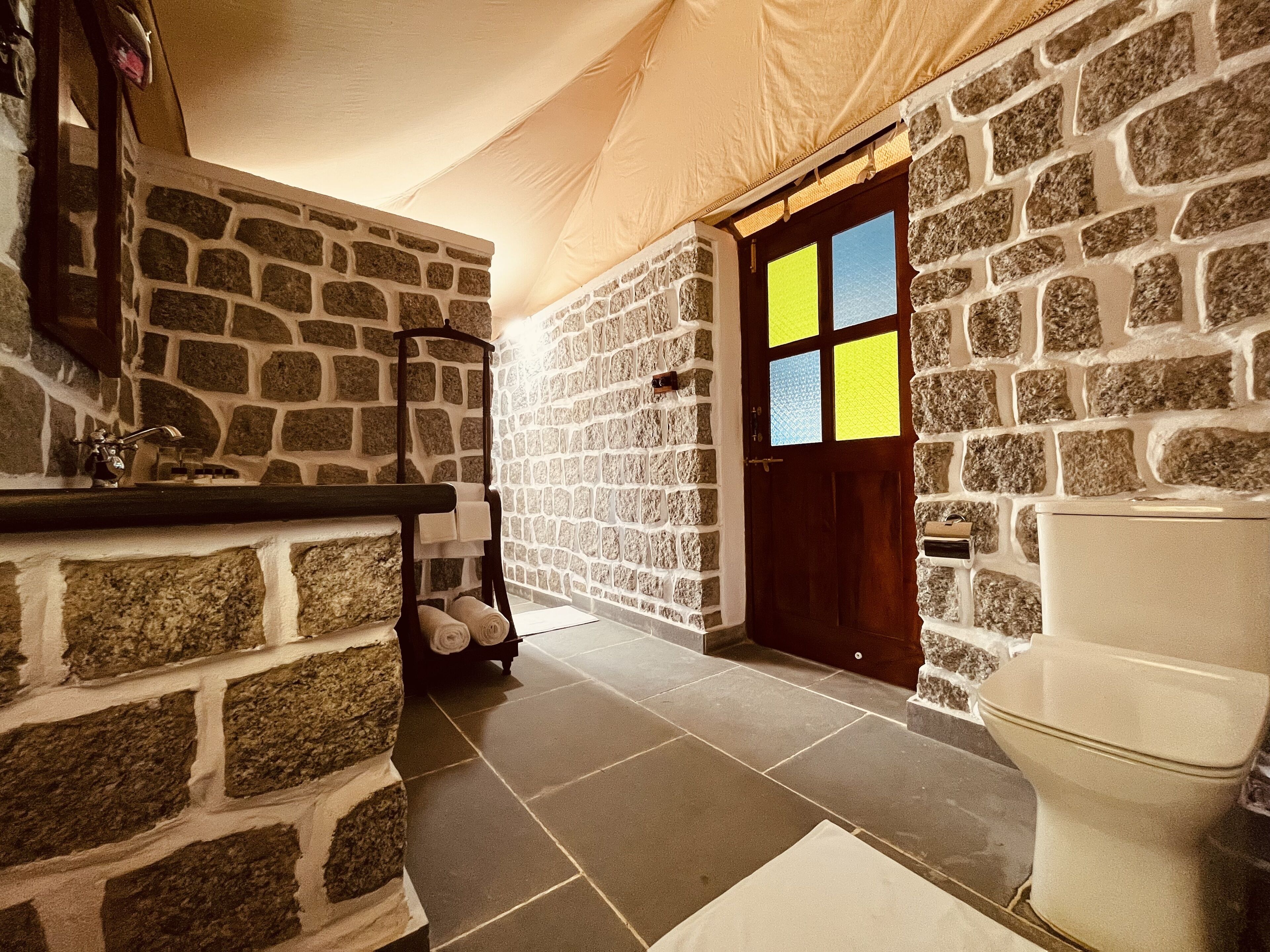 A stone-walled bathroom with a white toilet, a sink, and a towel rack.