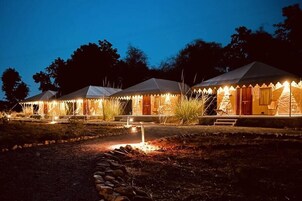 A row of tents with a well-lit entrance and a stone pathway leading to the main building.