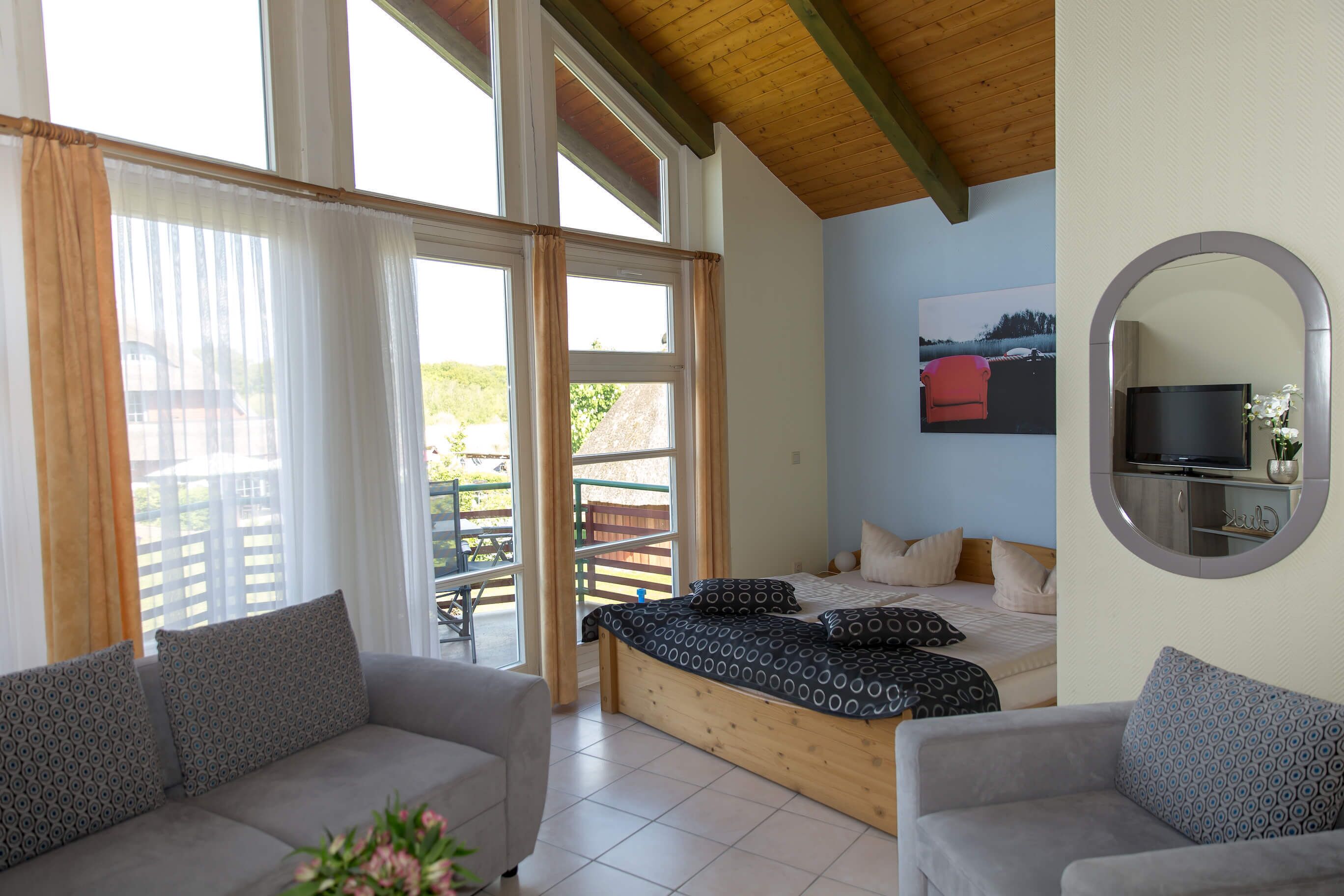Een slaapkamer met een bed, een slaapbank en een aan de muur bevestigde televisie.