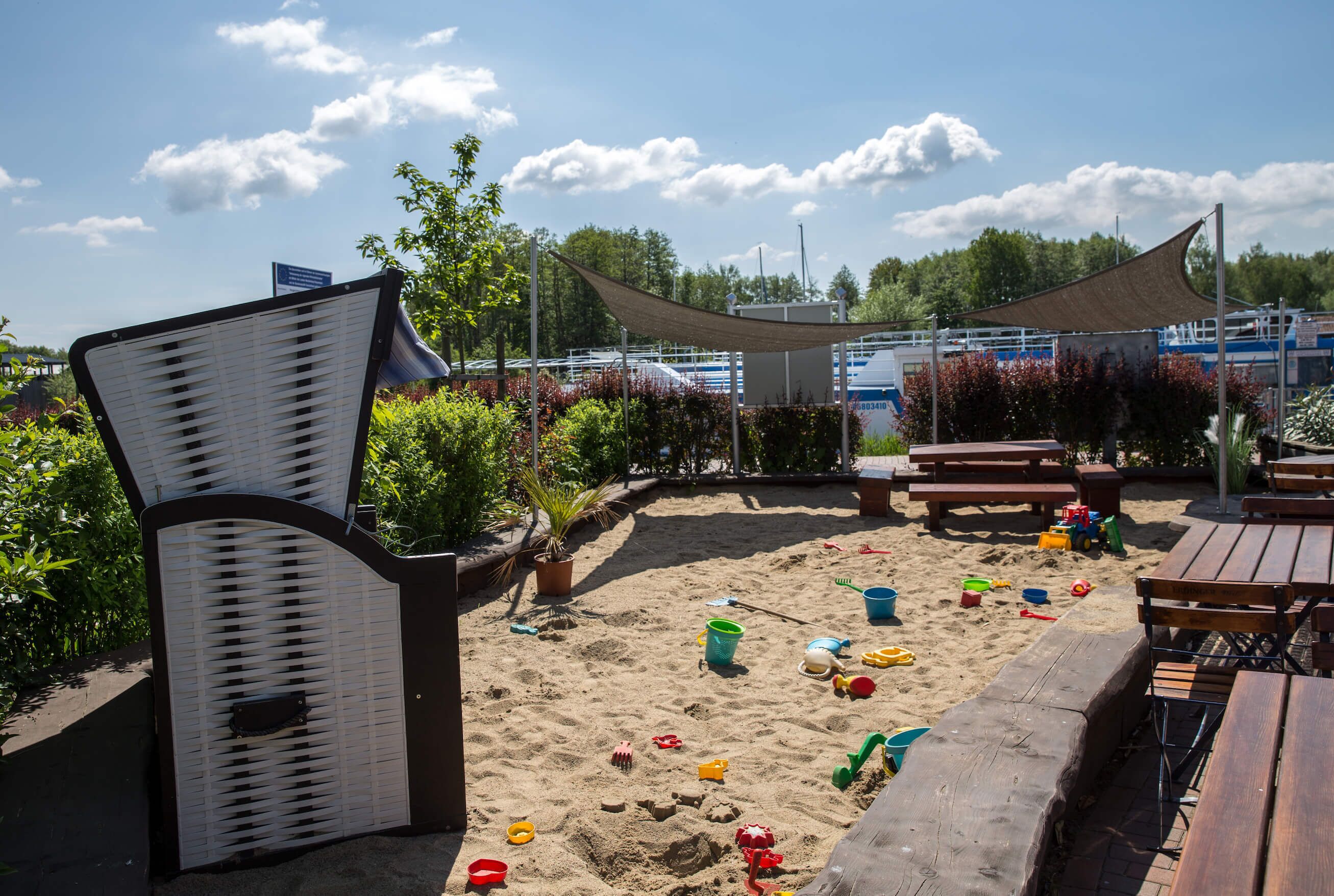 Ein Strandbereich mit Sand, Strandspielzeug und Holzliegen.