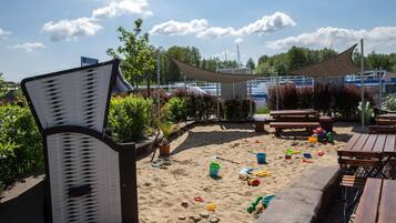 Ein Strandbereich mit Sand, Strandspielzeug und Holzliegen.
