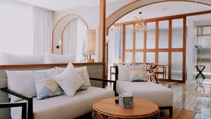 Una habitación de hotel moderna con un conjunto de sofá, una mesa redonda de madera y un ventanal con persianas.