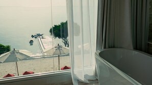Una habitación con vista a la playa, una bañera y una ventana con cortinas translúcidas.