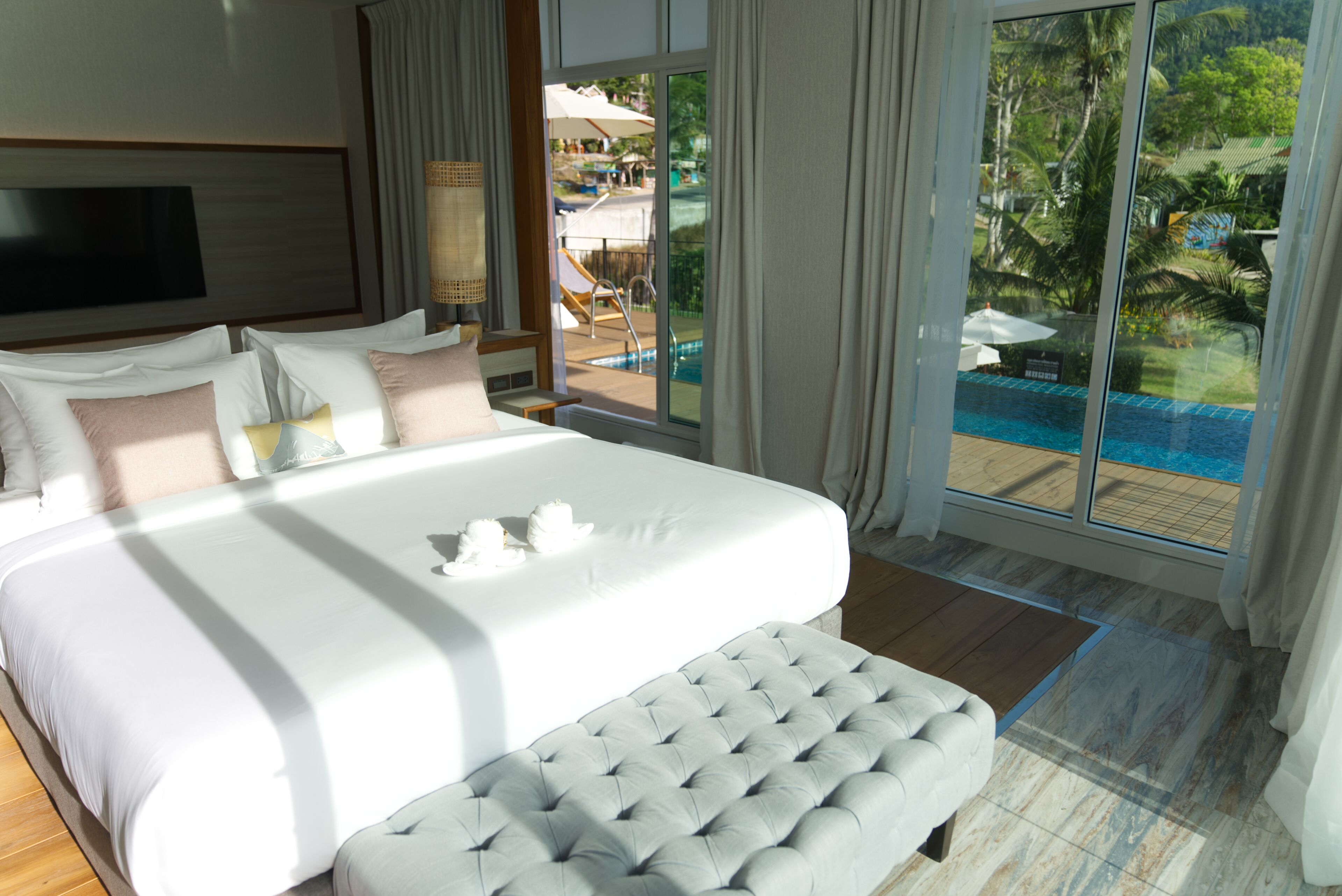 A hotel room with a large bed, a view of a pool, and a balcony with outdoor furniture.