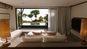 A modern bedroom with a large bed, a TV, and a view of a swimming pool and greenery. - Sichon Tesoro (Sichon)