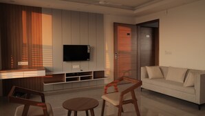 A modern living room with a flat-screen TV, wooden furniture, a sofa, and a ceiling fan. - The Presidential Suites (Bhuj)