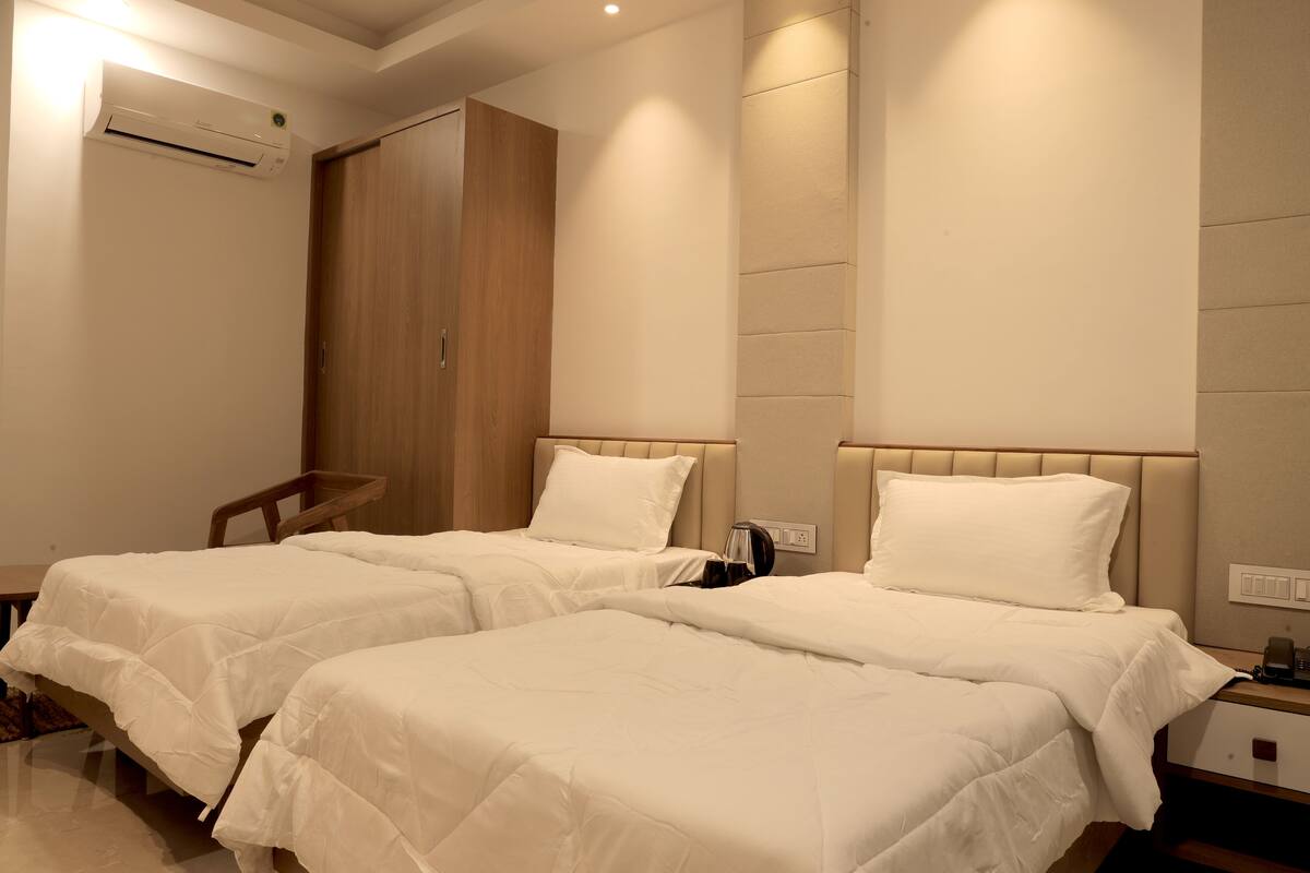 A hotel room with two single beds, a wooden wardrobe, an air conditioning unit, and a bedside table with a lamp.