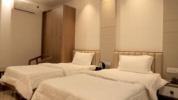 A hotel room with two single beds, a wooden wardrobe, an air conditioning unit, and a bedside table with a lamp.