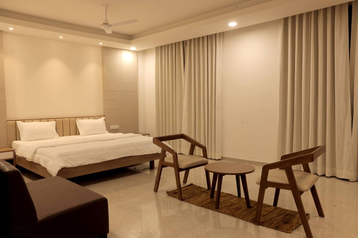 A modern hotel room with a large bed, two wooden chairs, a small table, and a ceiling fan.