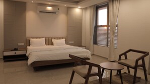 A modern bedroom with a large bed, bedside tables, a desk, and chairs. - The Presidential Suites (Bhuj)