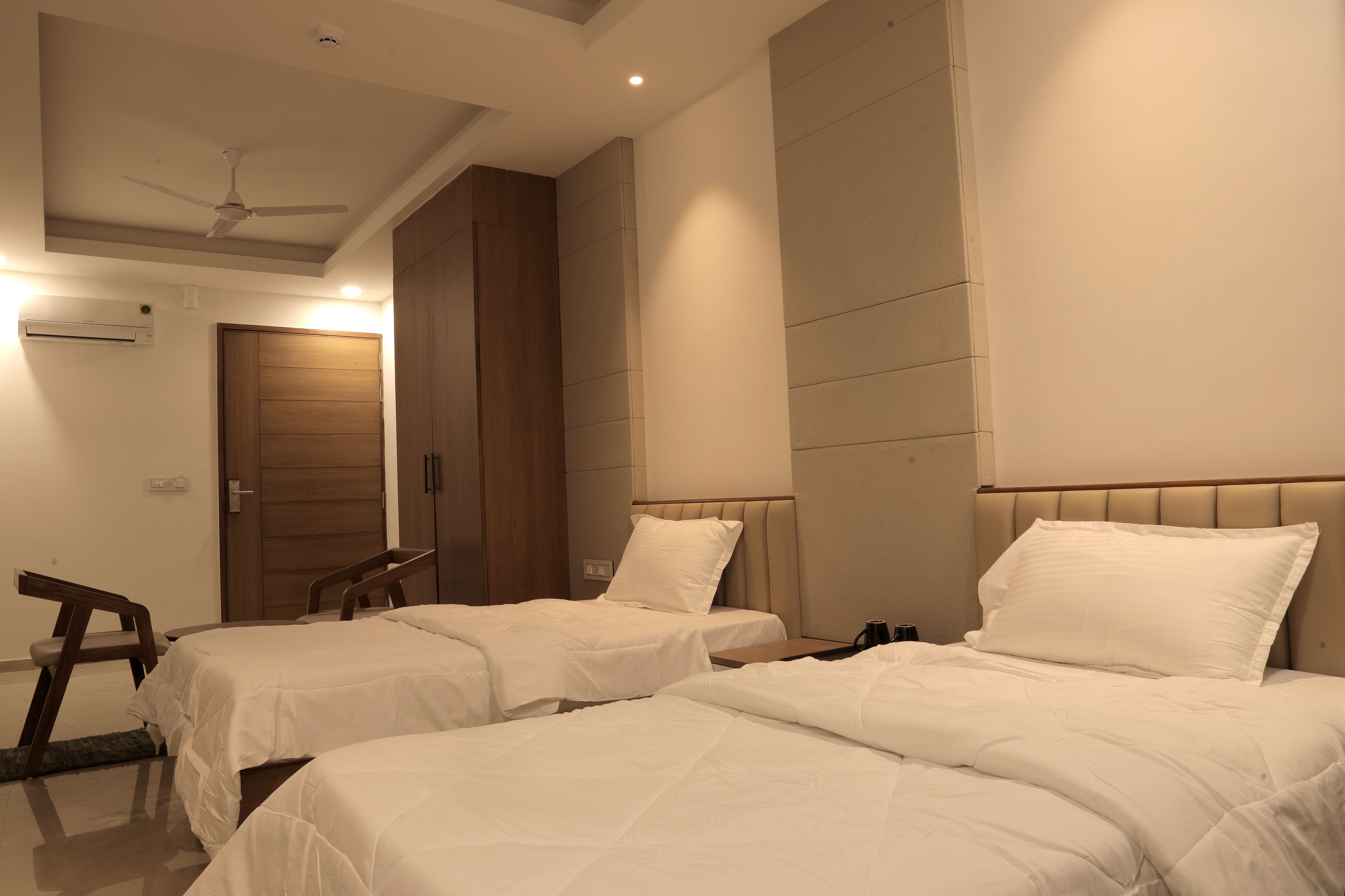 A hotel room with two single beds, a ceiling fan, an air conditioning unit, and a wooden wardrobe.