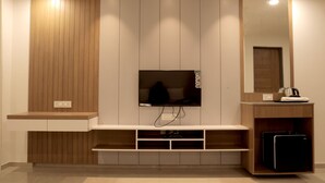 A modern living room with a flat-screen TV mounted on a wooden wall, a built-in coffee table, and a small cabinet with a mirror. - The Presidential Suites (Bhuj)