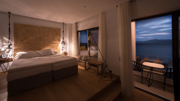 Ein Schlafzimmer mit einem großen Bett, Nachttischen, einer Bank und einem Balkon mit Stühlen und einem Tisch.