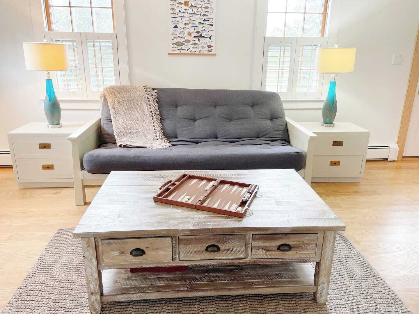 A living room with a grey sofa, two nightstands with lamps, a coffee table with a board game, and a wall art piece.