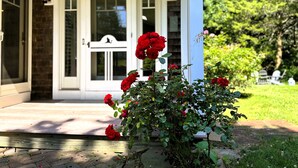 A house with a white front door, a porch, and a garden with red roses. - The Pet-Friendly Surf Shack Hideaway on the Cove (Eastham)