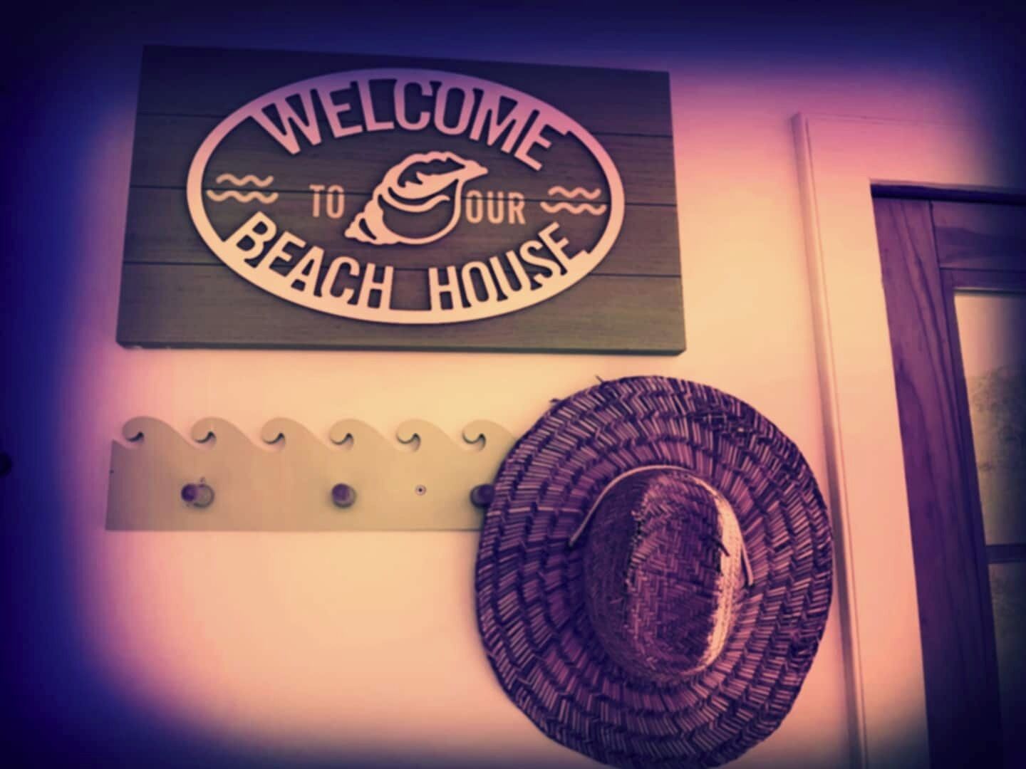 A 'Welcome to Your Beach House' sign and a woven beach hat on the wall.