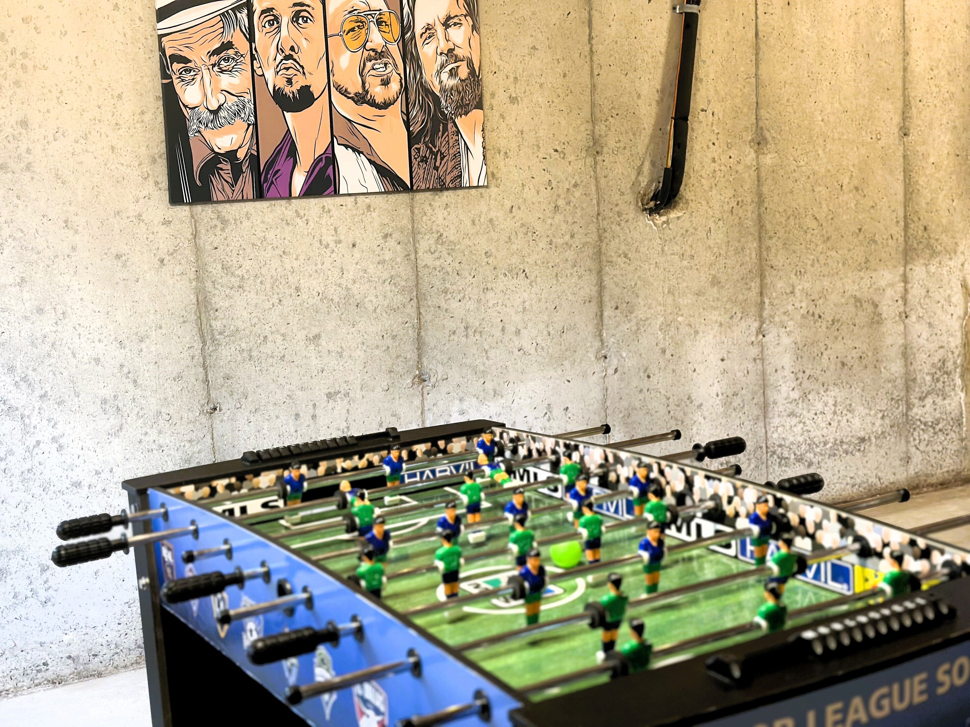 Une table de baby-foot dans une pièce avec un mur en béton et une affiche d’une équipe de football.