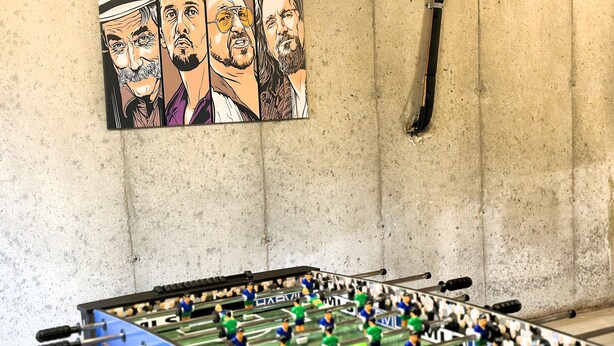 Een tafelvoetbaltafel in een ruimte met een betonnen muur en een poster van een voetbalteam.