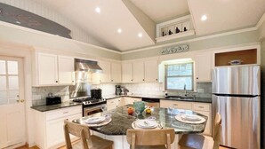 A modern kitchen with white cabinets, a stainless steel stove, and a refrigerator. - The Pet-Friendly Surf Shack Hideaway on the Cove (Eastham)