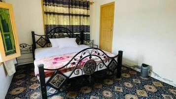 Un dormitorio con cama, ventilador de techo, baldosas de suelo estampadas, ventana con cortinas y una puerta.