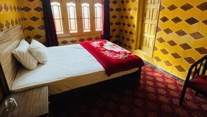 Una habitación con cama, una silla, ventilador de techo y ventana con cortinas.